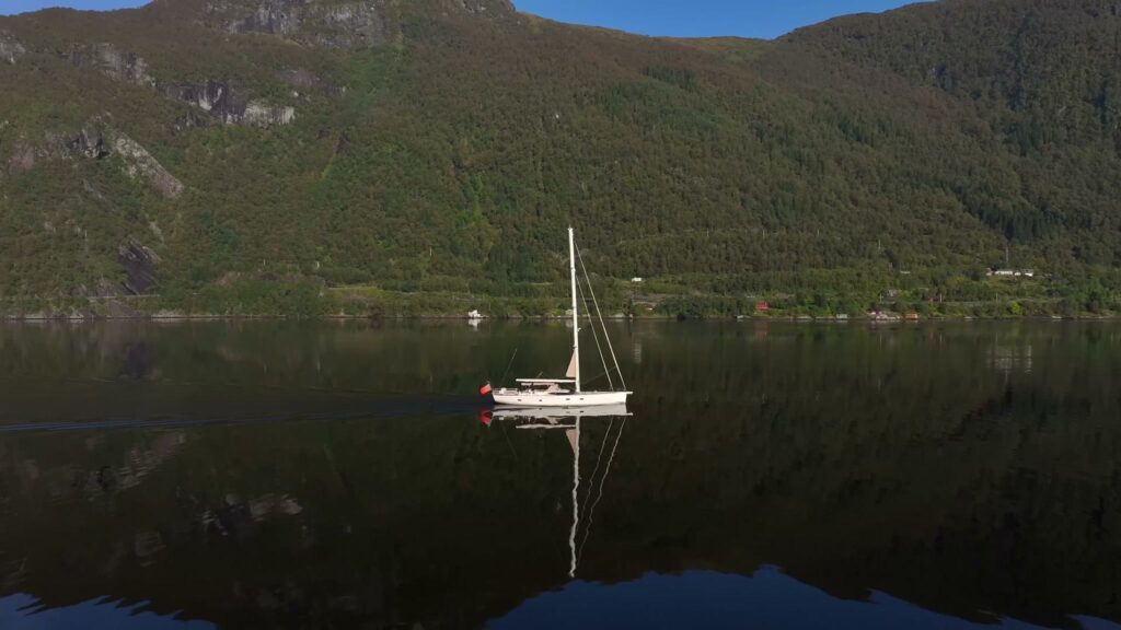 Sailing yacht in a Norwegian fjord past red boathouses